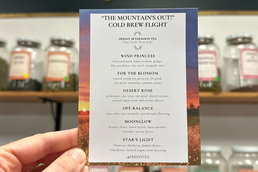 Menu card for 'The Mountains Out' Cold Brew Flight held by a hand with blurred jars in the background