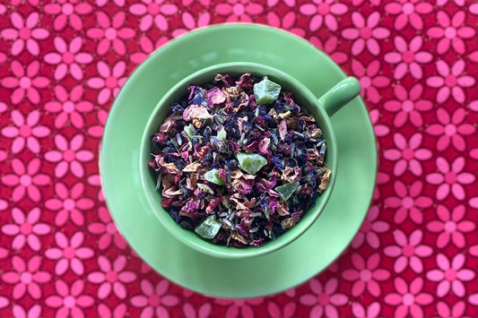 green teacup full of fruits and flowers on a pink flower backdrop