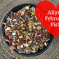 Bowl of dried herbs with a red heart-shaped card reading 'Allyn's February Pick!' on a textured surface.