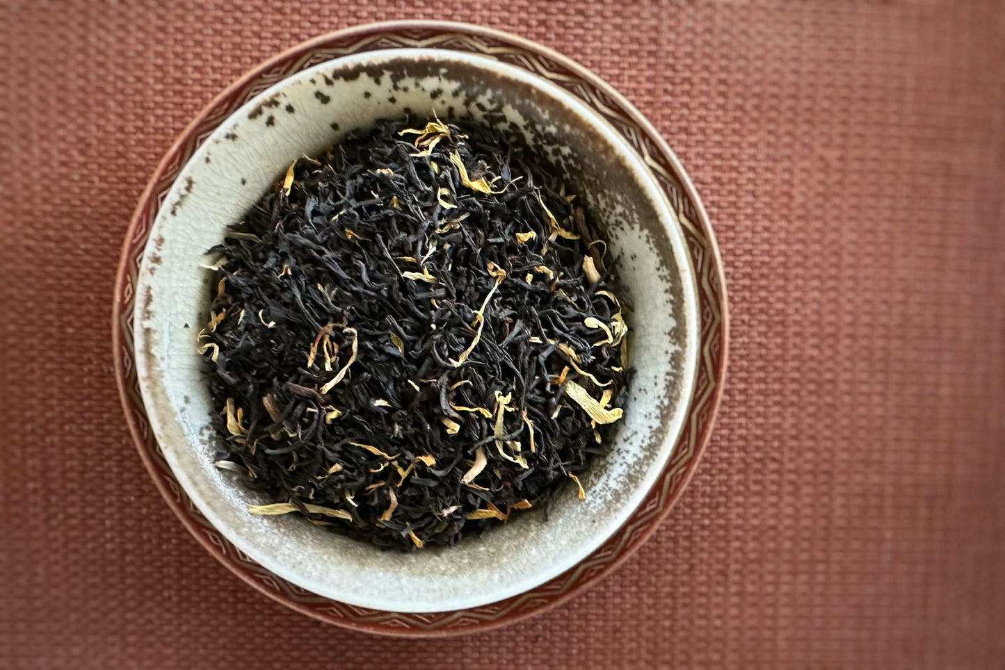 Earthen-tone dish full of black tea leaves with marigold petals