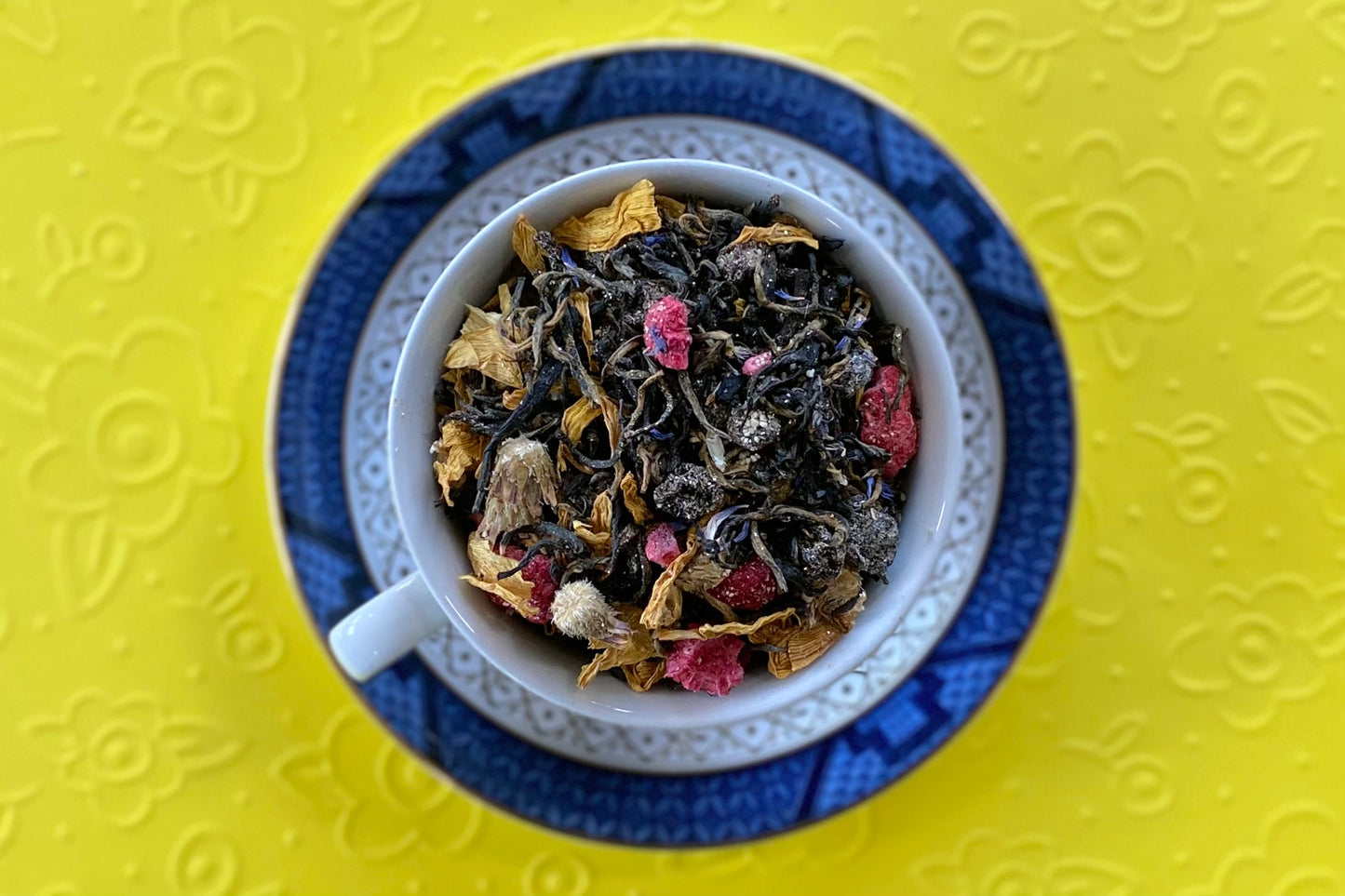 Blue teacup full of fruits, flowers and tea leaves on yellow background 