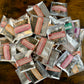 A pile of small silver-backed windowed pouches containing loose herbal tea samples