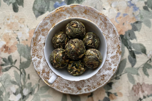 A white and gold teacup full of pressed white tea balls with jasmine flowers