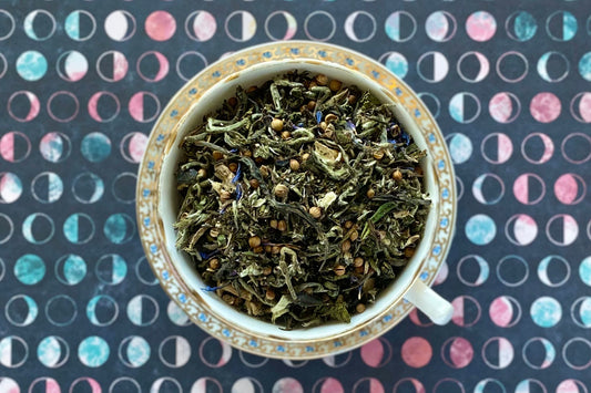 Blue and white teacup full of white tea with coriander and blue flowers