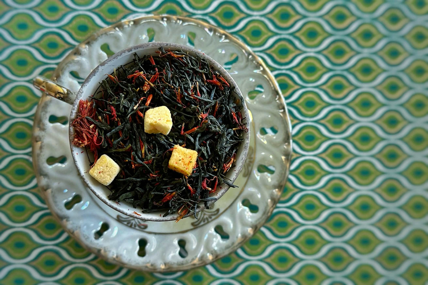 Teacup full of deep green tea with chunks of mango and feathery red safflower petals