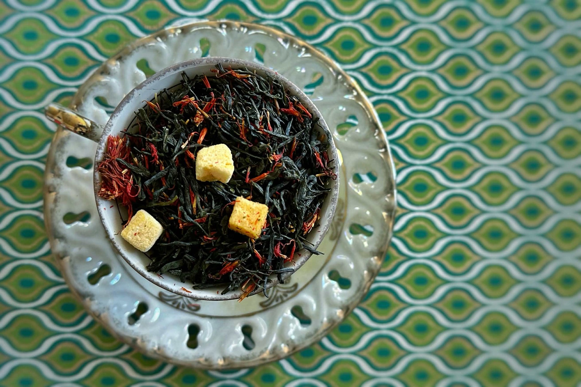 Teacup full of deep green tea with chunks of mango and feathery red safflower petals