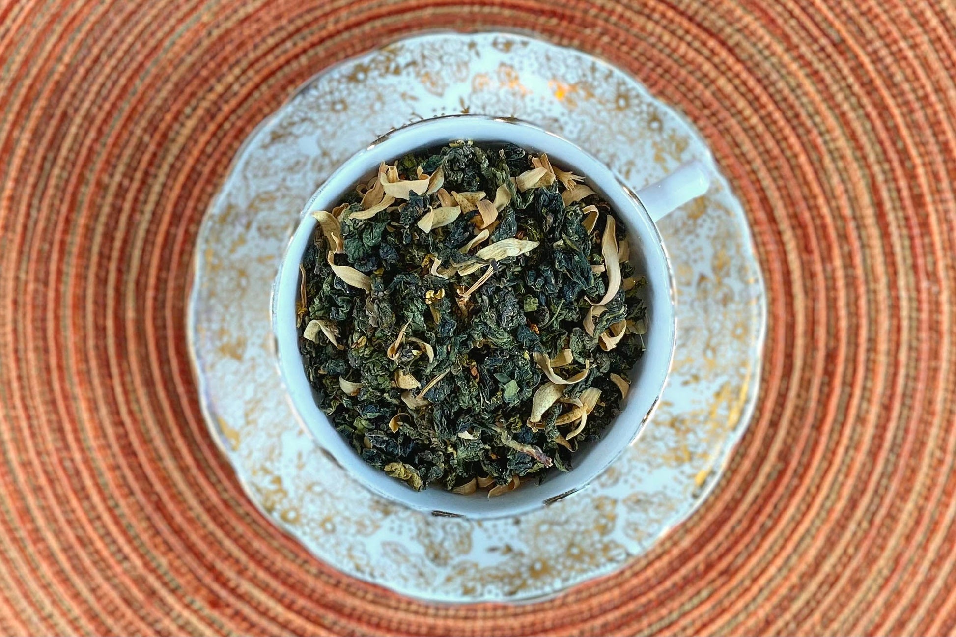 teacup full of rolled oolong leaf with orange blossoms and gold glitter