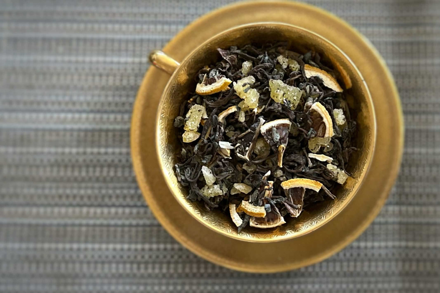 Gilded teacup full of aged black tea with chunks of crystalized ginger and dried lemon