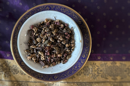 Teacup full of gold and black tea with peppercorns and purple glitter