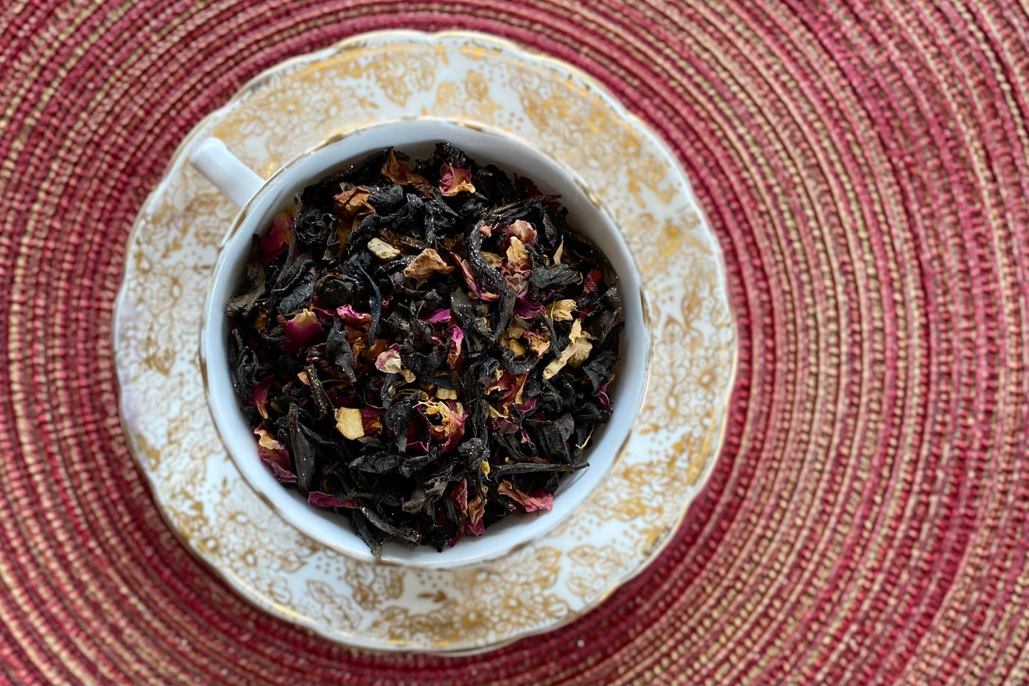 teacup full of dark oolong tea with rose petals and gold glitter