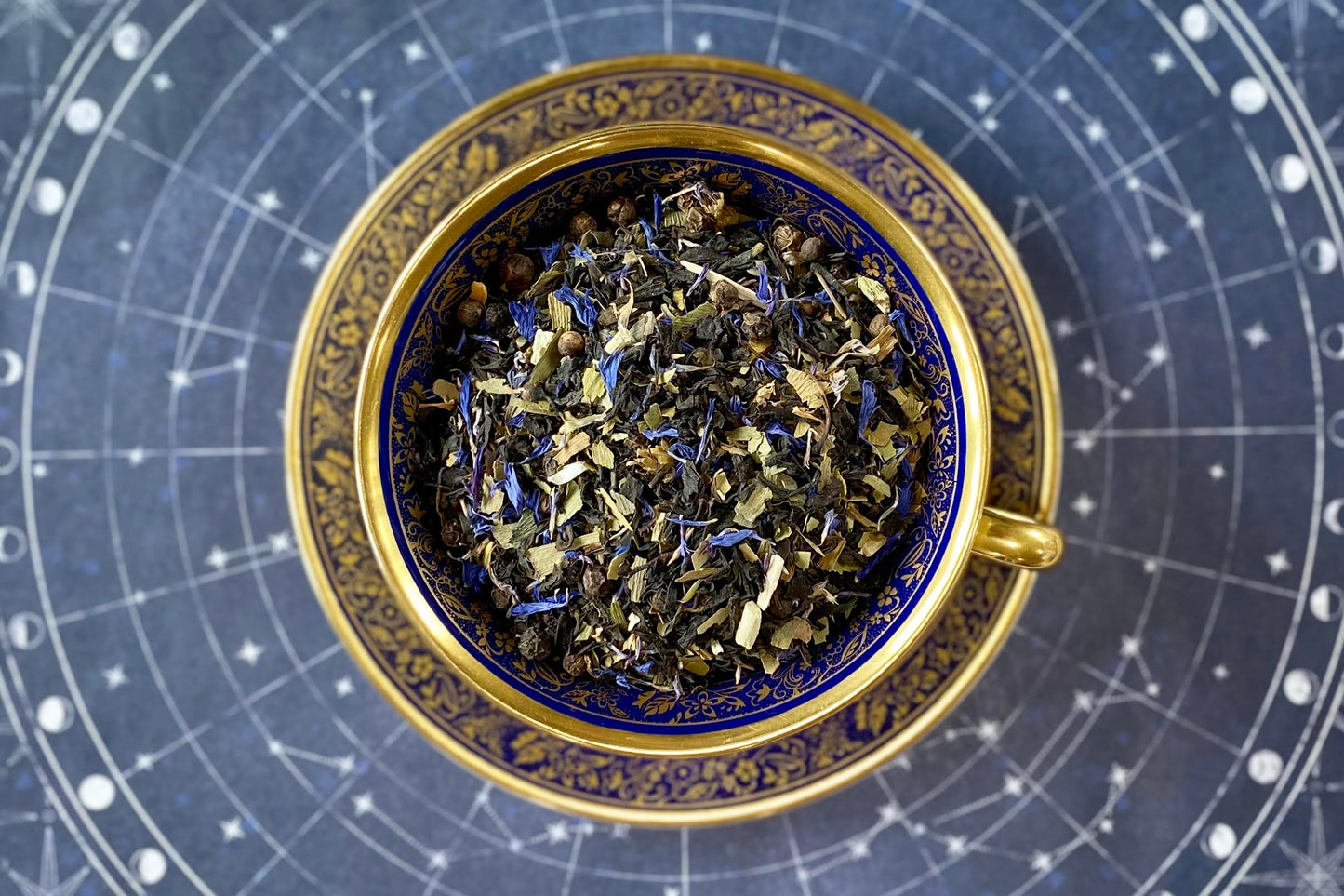 teacup full of black and green leaves with blue flowers