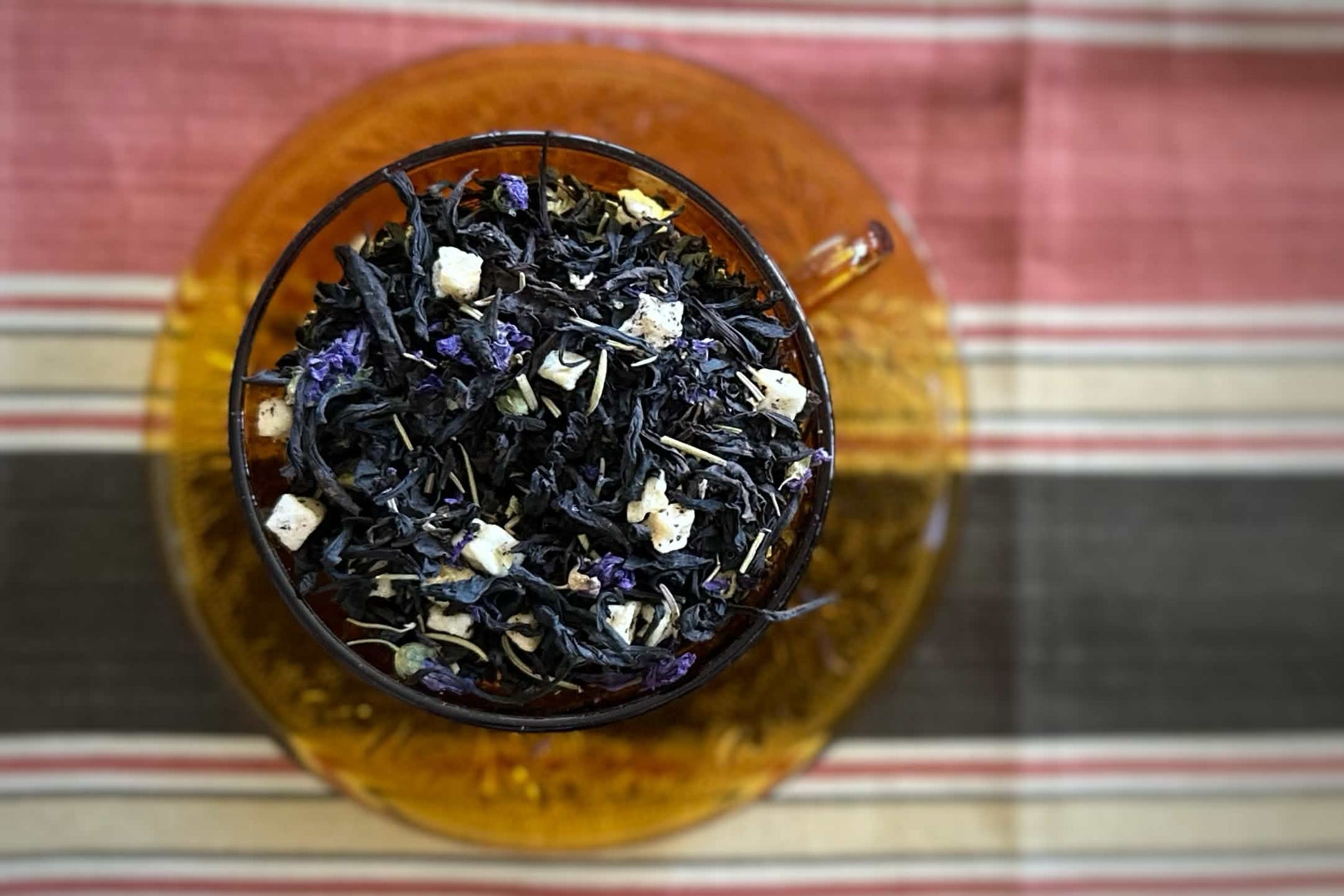 Teacup full of wiry dark oolong tea with apple, rosemary and blue flowers