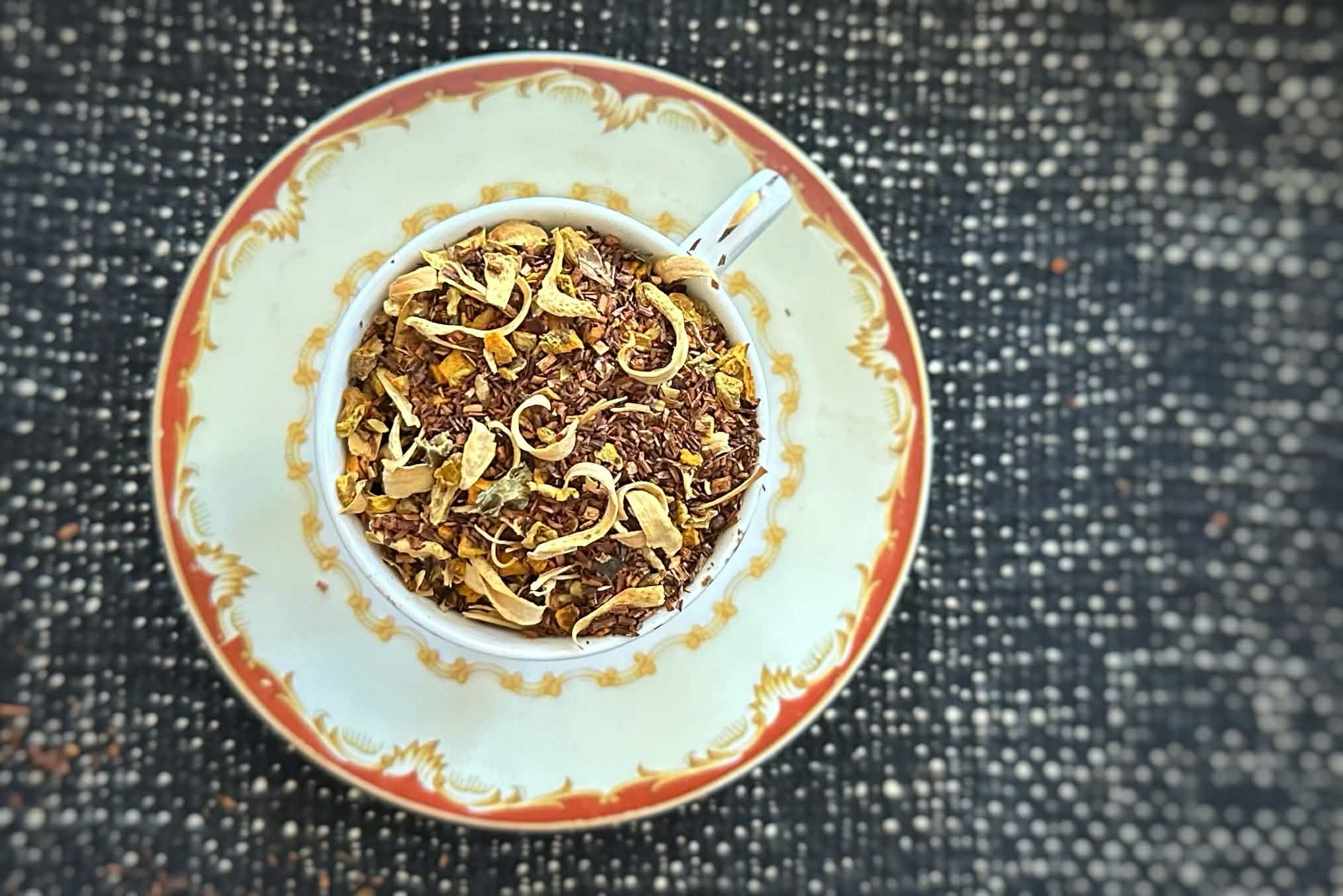 Teacup full of rooibos red tea with orange blossom curls and yellow chips of turmeric