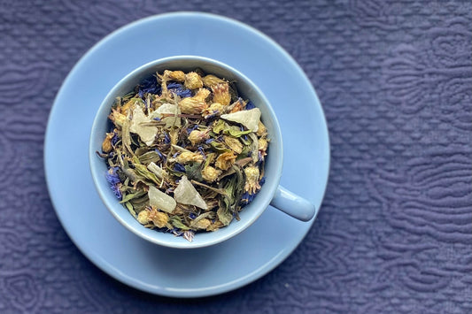 teacup full of white tea, aloe pieces and blue flowers