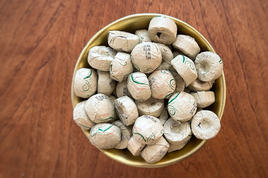 Gold bowl filled with small foil-wrapped tea cakes on a wooden surface