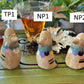 Three pigeon tea pets with colored ruffs one with trans flag coloring labeled TP1, two with nonbinary flag coloring labeled NP1 and NP2