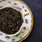 A cup of dry oolong tea leaves placed on a saucer with floral patterns, on a dark textured background.